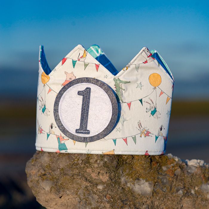 Corona de cumpleaños infantil hecha a mano en tela de algodón con animalitos y número 1, ideal para celebrar el primer cumpleaños de un bebé.