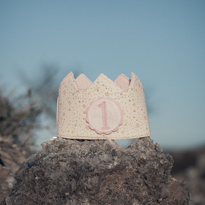 Corona de cumpleaños infantil de tela hecha a mano con estampado de estrellas y número 1 intercambiable, colocada sobre una piedra al aire libre.