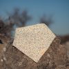 Bandana para bebé hecha a mano con estampado floral sobre fondo claro, colocada sobre una piedra al aire libre.