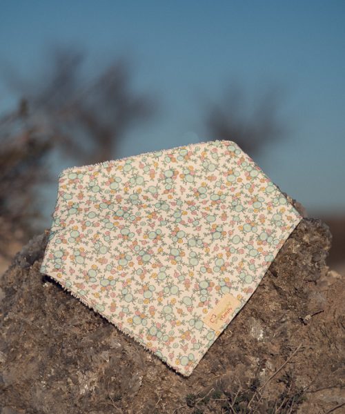 Bandana para bebé hecha a mano con estampado floral sobre fondo claro, colocada sobre una piedra al aire libre.