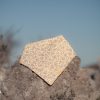 Bandana para bebé hecha a mano con estampado de pequeñas flores silvestres sobre fondo claro, colocada sobre una piedra al aire libre.