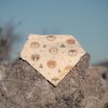 Bandana para bebé hecha a mano con estampado de animales del bosque sobre fondo beige, colocada sobre una piedra al aire libre.