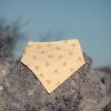 Bandana para bebé hecha a mano con estampado de pequeñas flores amarillas sobre fondo crema, colocada sobre una piedra al aire libre.