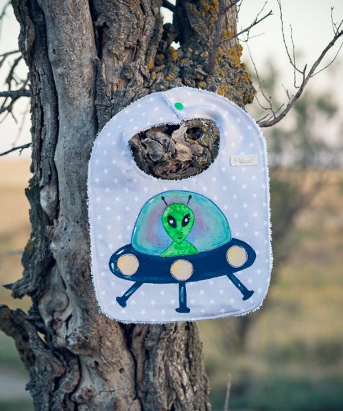 Babero infantil artesanal con aplicación de un extraterrestre en una nave espacial.