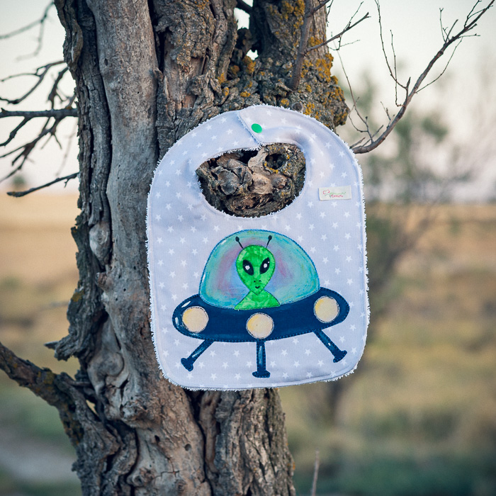 Babero infantil artesanal con aplicación de un extraterrestre en una nave espacial.