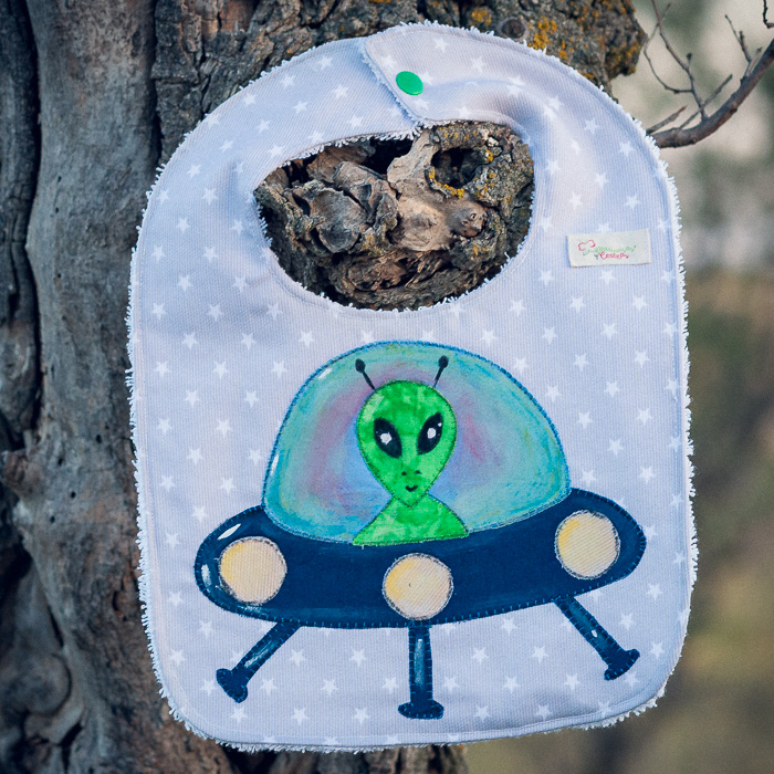 Babero infantil artesanal con aplicación de un extraterrestre en una nave espacial.