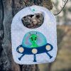 Babero infantil artesanal con aplicación de un extraterrestre en una nave espacial.