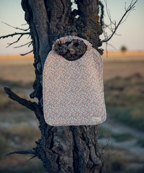 Babero de mesa infantil con estampado de pequeñas flores rosas y cuello elástico.