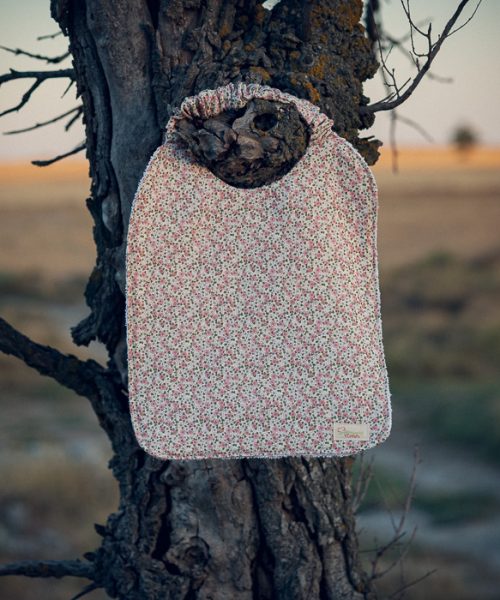Babero de mesa infantil con estampado de pequeñas flores rosas y cuello elástico.
