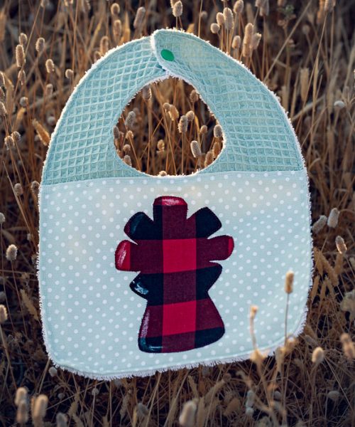 Babero infantil artesanal con aplicación de la Virgen del Pilar en tela de cachirulo y gofre verde.