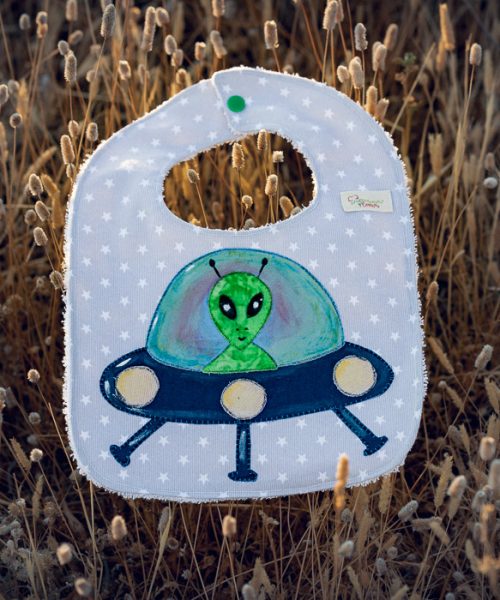Babero infantil artesanal con aplicación de un extraterrestre en una nave espacial.