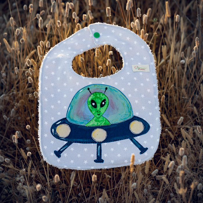 Babero infantil artesanal con aplicación de un extraterrestre en una nave espacial.