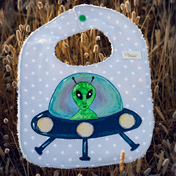 Babero infantil artesanal con aplicación de un extraterrestre en una nave espacial.