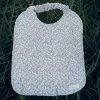 Babero de mesa infantil con estampado de pequeñas flores rosas y cuello elástico.