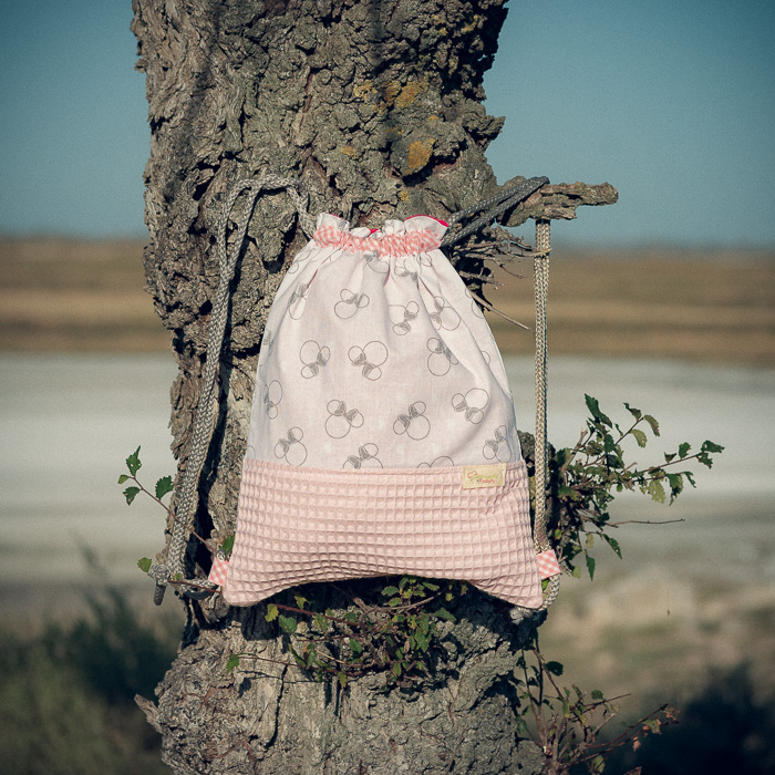 Mochila infantil pequeña de tela con estampado de lazos sobre fondo rosa hecha a mano.