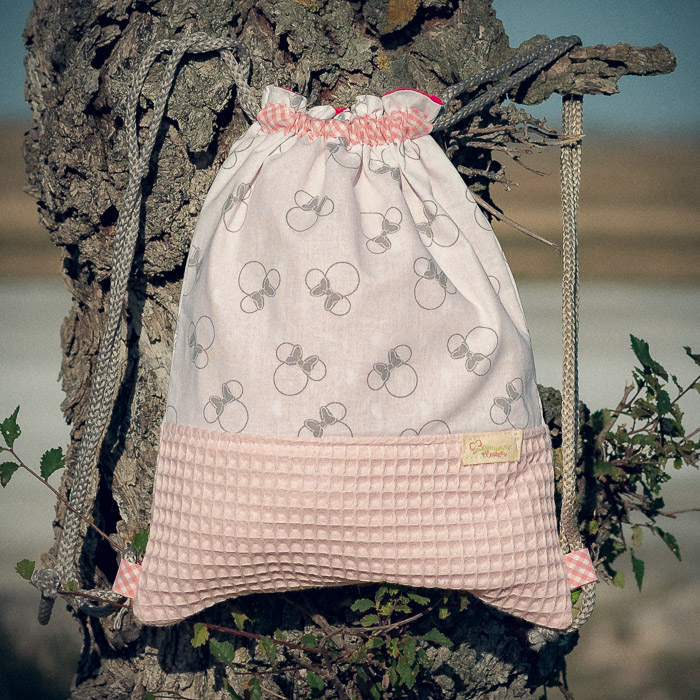 Mochila infantil pequeña de tela con estampado de lazos sobre fondo rosa hecha a mano.