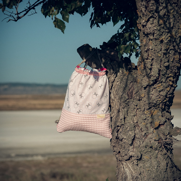 Mochila infantil pequeña de tela con estampado de lazos sobre fondo rosa hecha a mano.