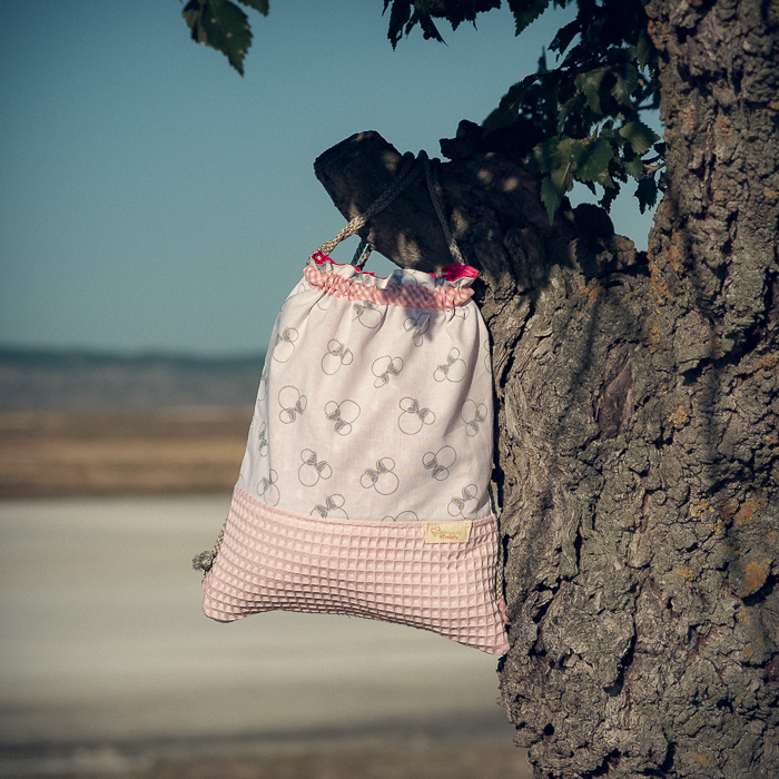 Mochila infantil pequeña de tela con estampado de lazos sobre fondo rosa hecha a mano.